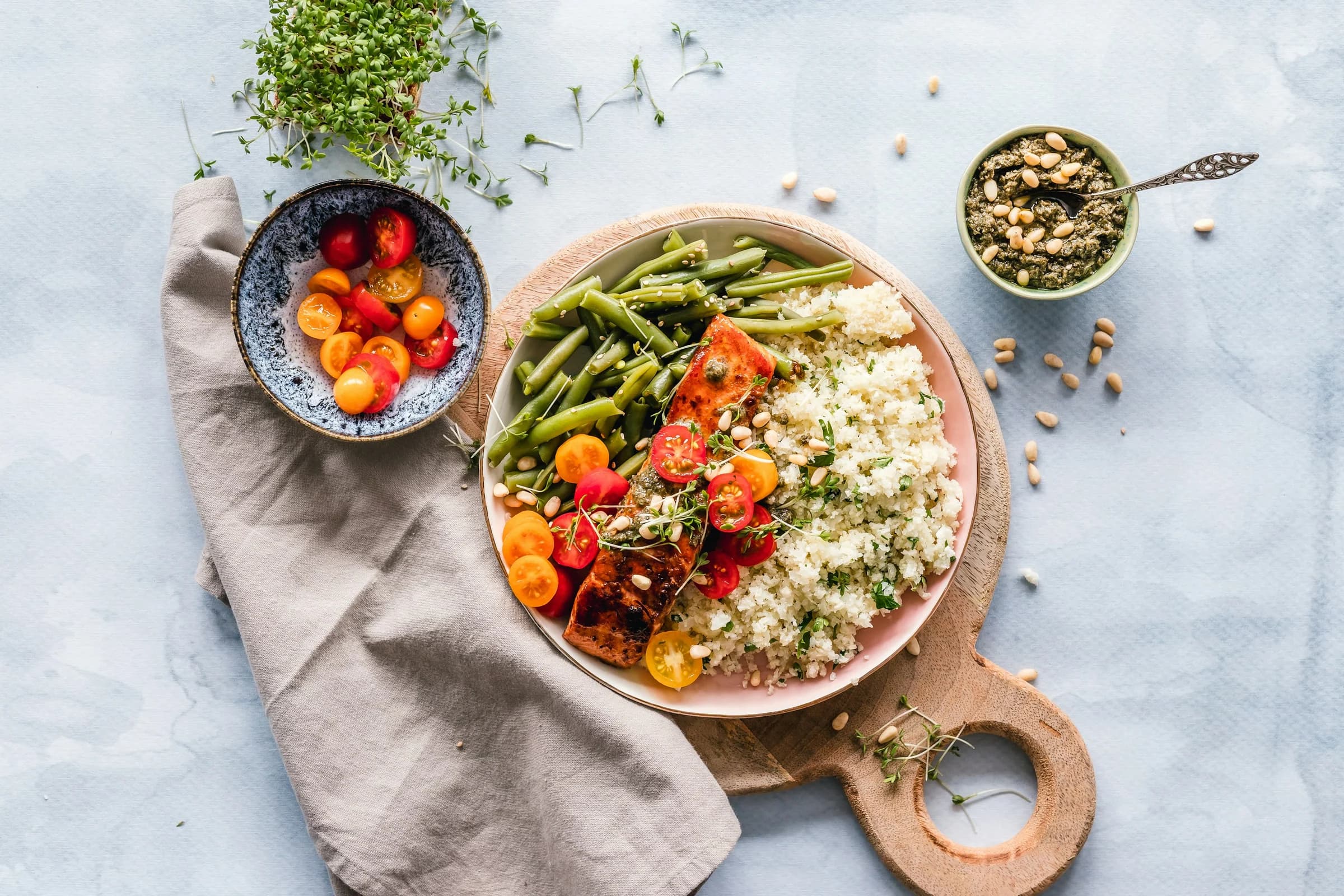 Salmon with green beans, tomatoes, grains and pesto on a colorful plate.