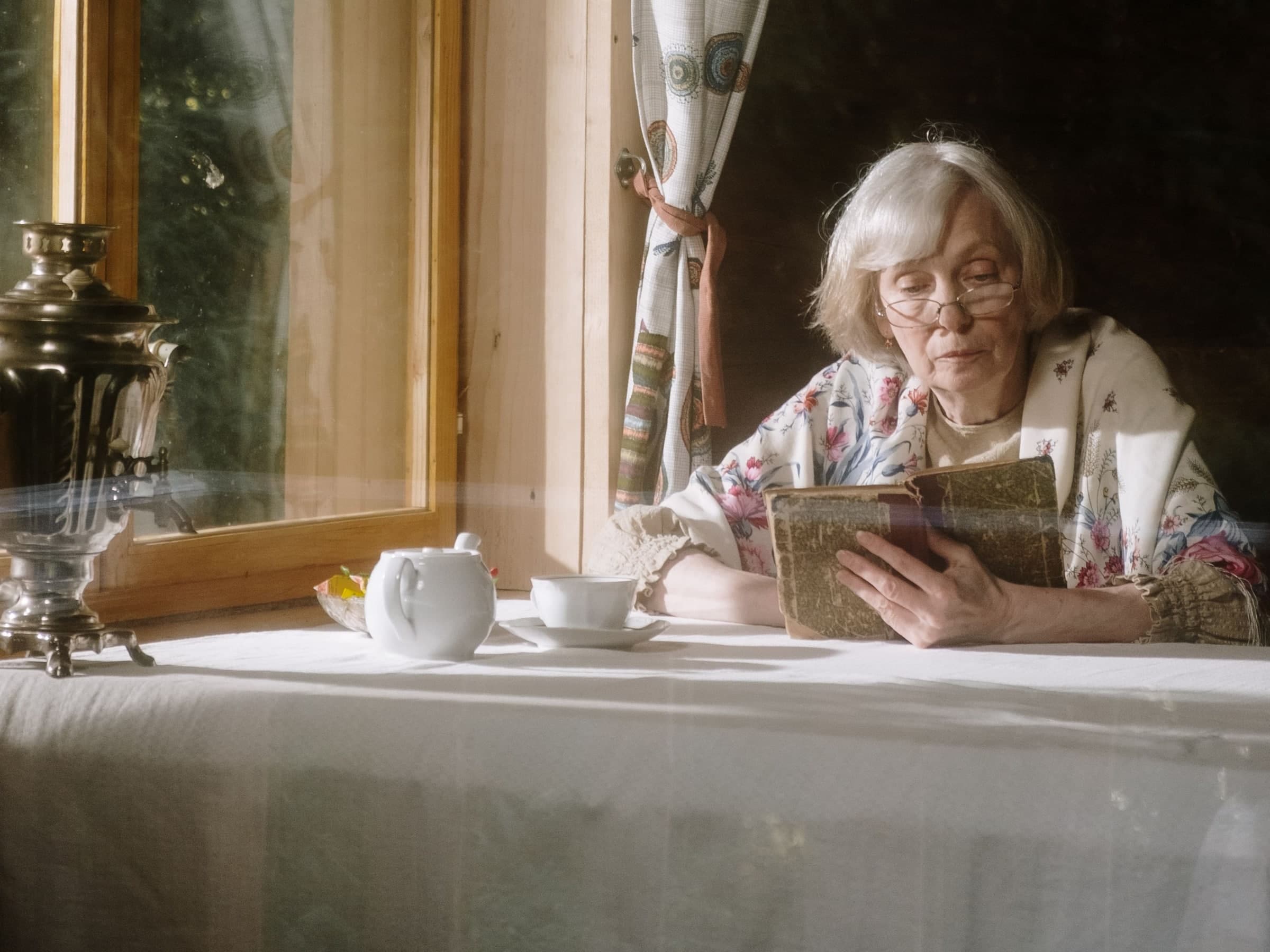 Mature woman reading comfortably with glasses in daylight.