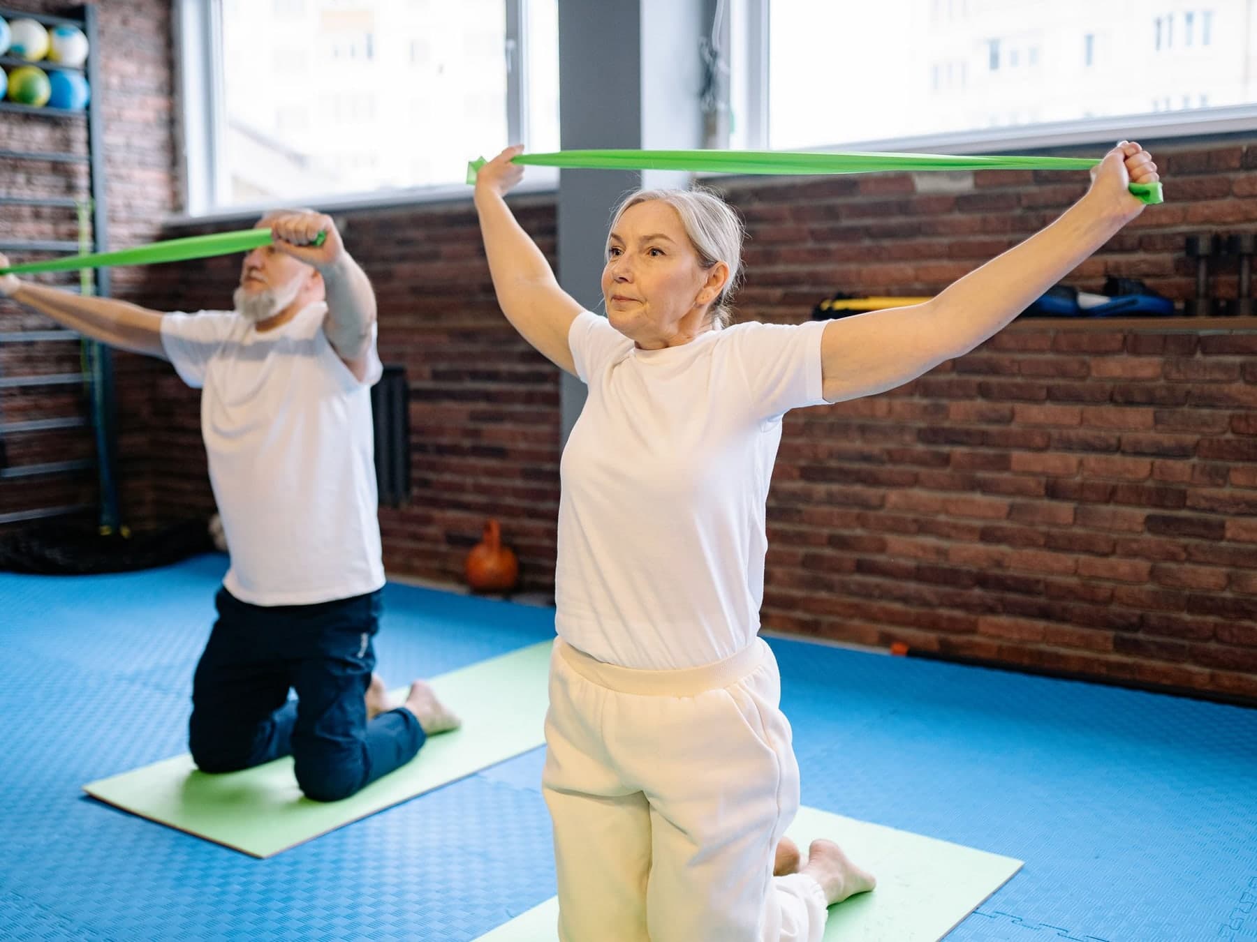 Older man and woman doing resistance-band exercises on mats in a gym