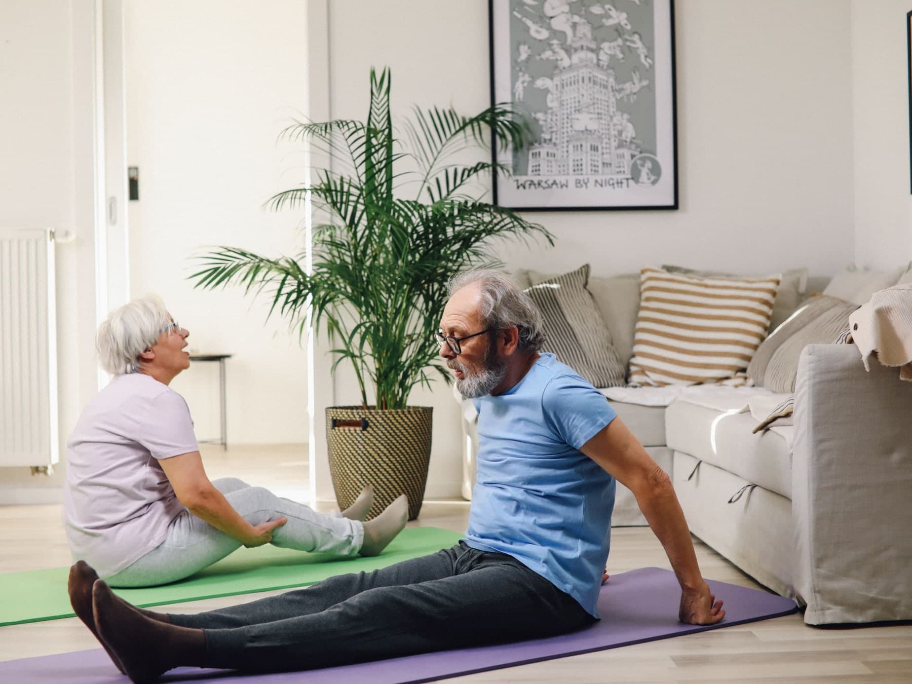 Older man and woman stretching on yoga mats in a living room