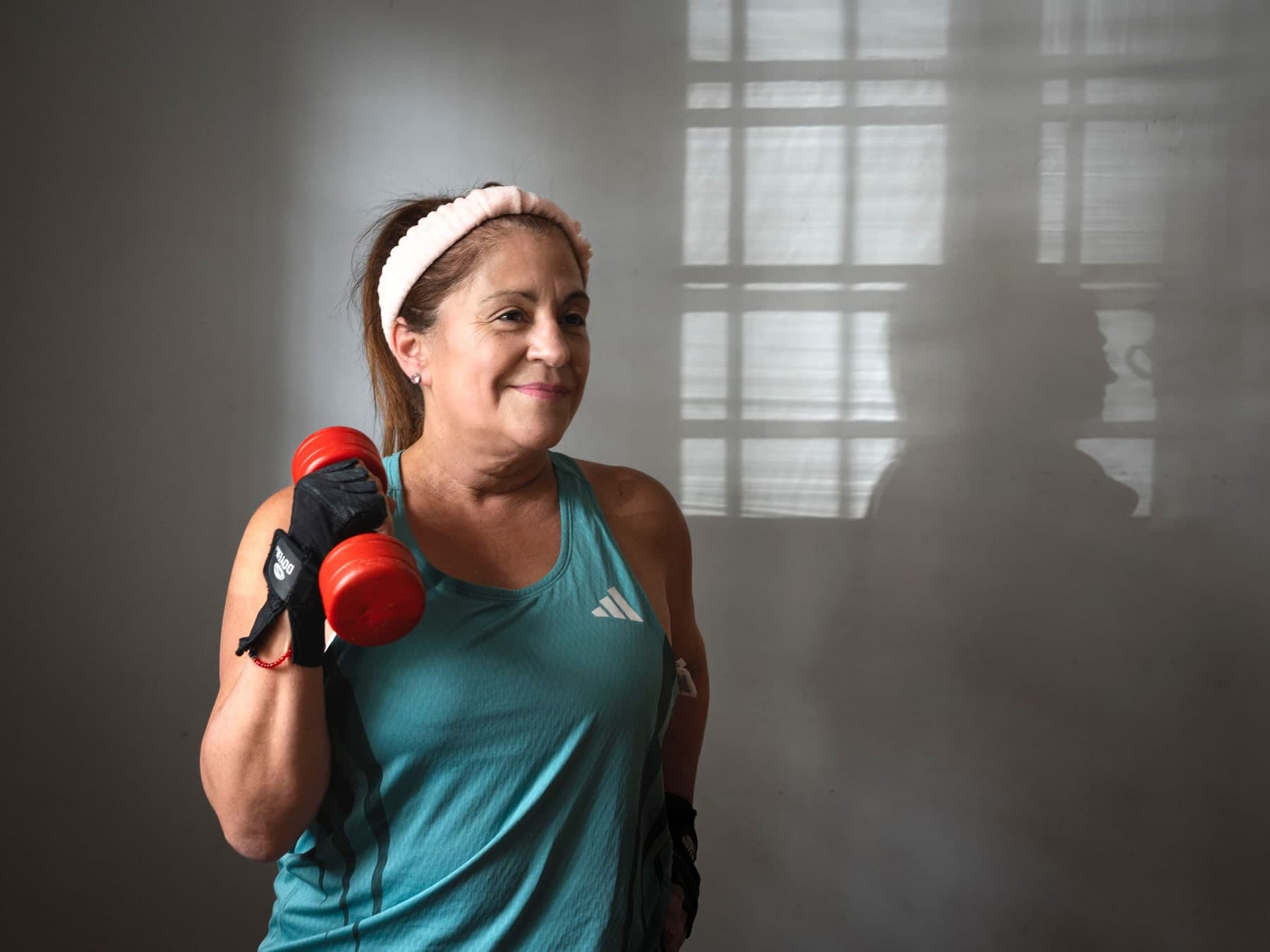 Older woman in a teal workout top holding a red dumbbell at her shoulder