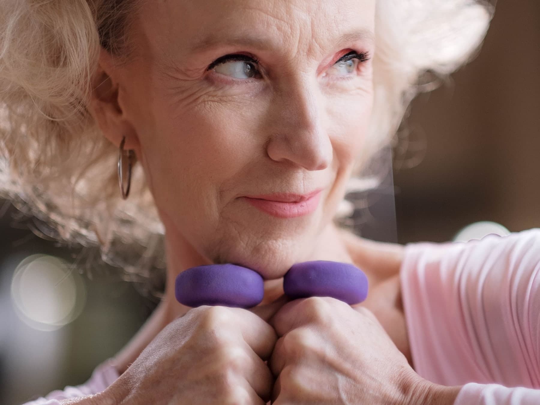 Older woman with white hair holding small purple dumbbells in front of her chest